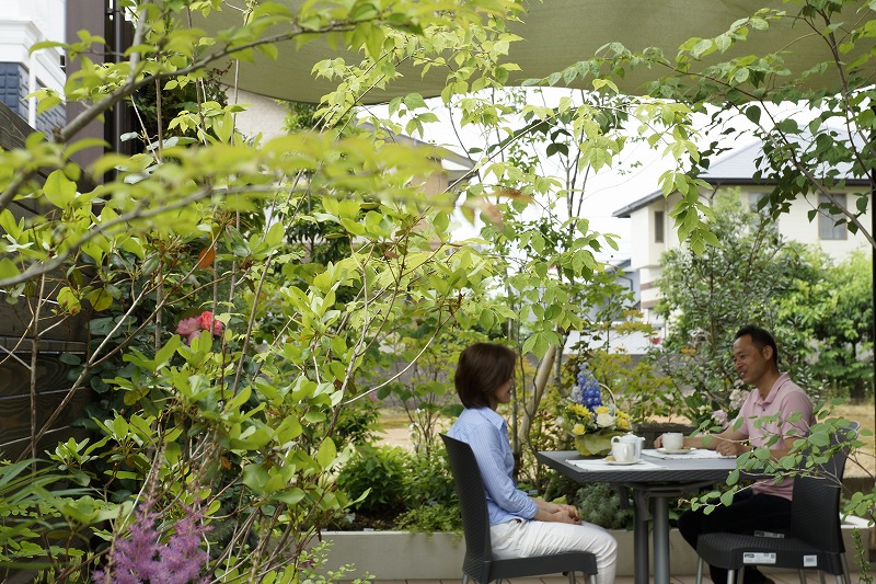 パーゴラ下でテーブルを囲み会話を楽しむ家族の姿。