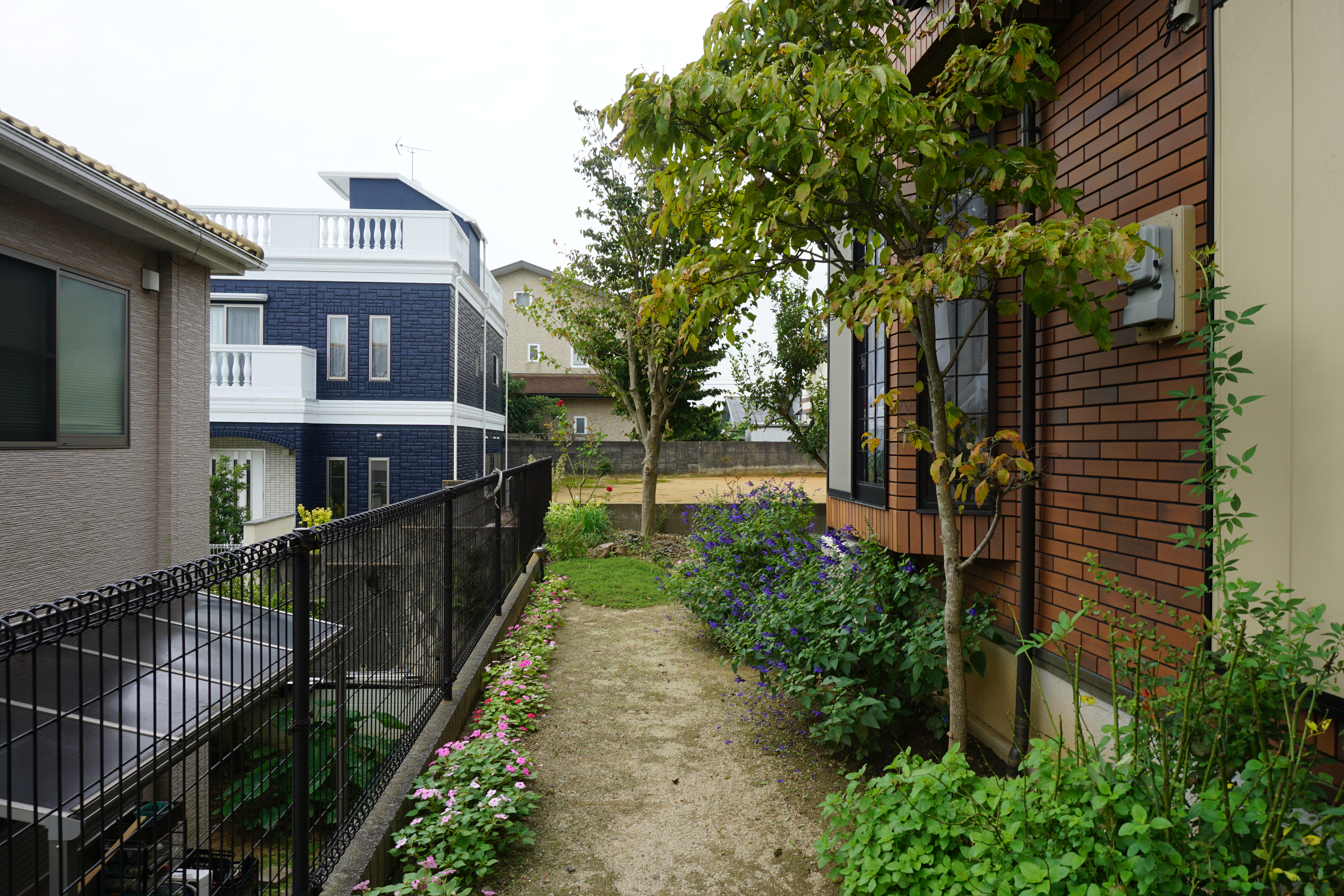 リフォーム前の庭通路。土の地面と既存フェンスが続く細長いスペース。