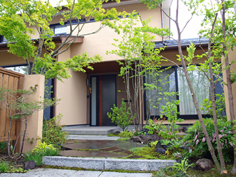 自然石貼りのアプローチにモミジの枝葉がかかる玄関前の景色。