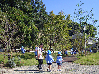 芝生と雑木に包まれた園庭で、園児たちが遊ぶ完成後の広場。