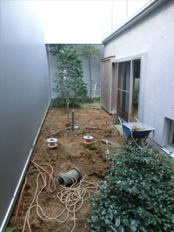 施工前のアプローチからの眺め。土の地面とコンクリート壁が続く。