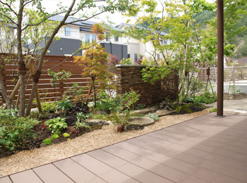 下草と砂利のコントラストが美しい庭。雑木が優しい影を落とし、ウッドフェンスで目隠ししながらすっきりと整えられた様子。