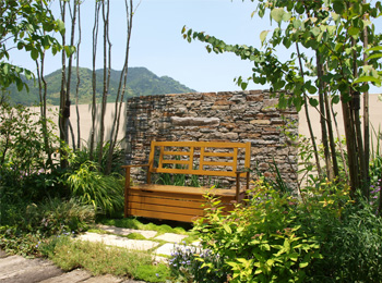 石積みの壁とベンチを配した、緑に囲まれた落ち着いたコーナーガーデンの施工後。