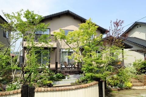 樹木と草花に包まれた、明るいウッドデッキまわりの外観。