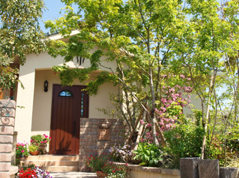 施工後のアプローチ。洋風の建物の外観に似合う、雑木とレンガが調和した玄関前の庭。