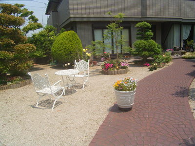 リフォーム前の玄関アプローチ。砂利敷きに白いテーブルとイスが置かれた様子。