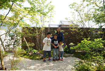 ご家族と愛犬が庭で並んで立つ記念写真。雑木と壁を背景にした一枚。